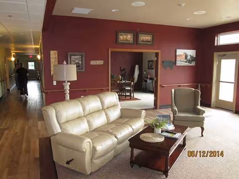 Cozy senior living lounge with beige sofa, chair, coffee table, and burgundy walls.