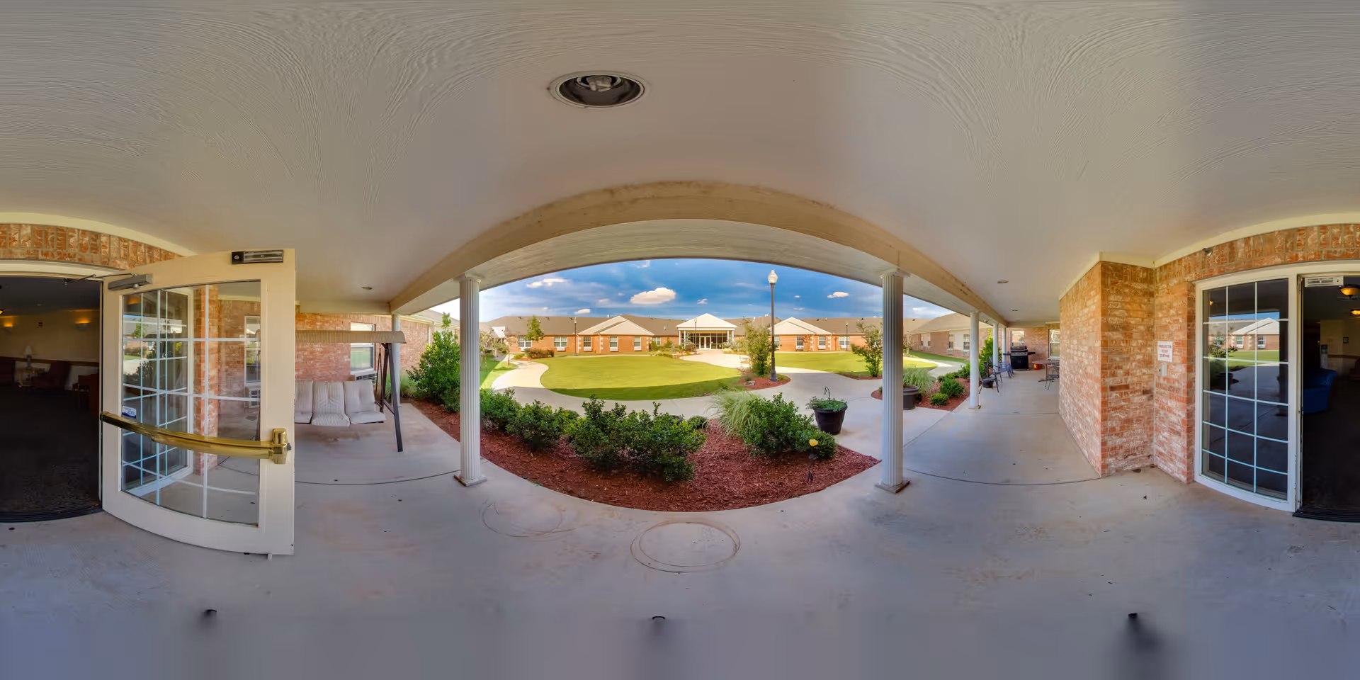 Covered entrance walkway with columns overlooking a landscaped central courtyard and surrounding brick nursing center buildings.