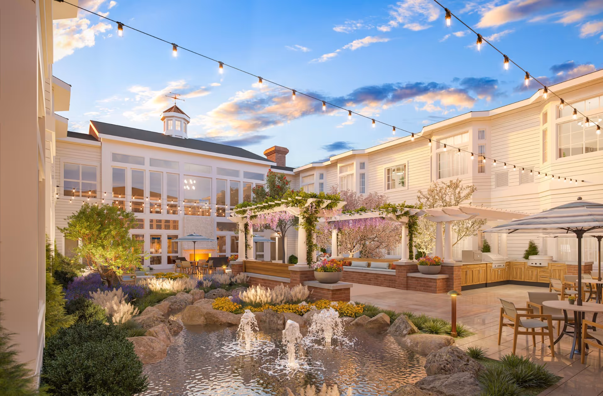 Courtyard of a senior living facility with a decorative pond and fountains, string lights, pergola, outdoor seating and landscaping.