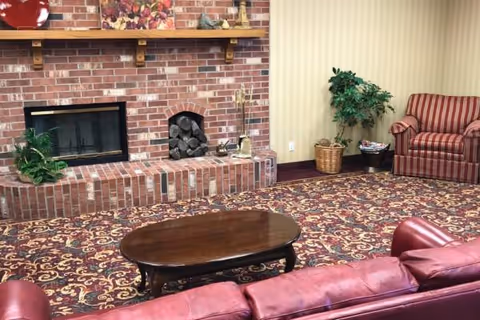 Cozy living room with brick fireplace, patterned carpet, and red leather seating.