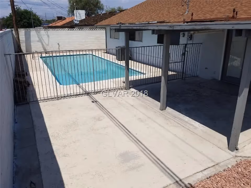 Small fenced backyard swimming pool beside a covered patio and concrete deck.