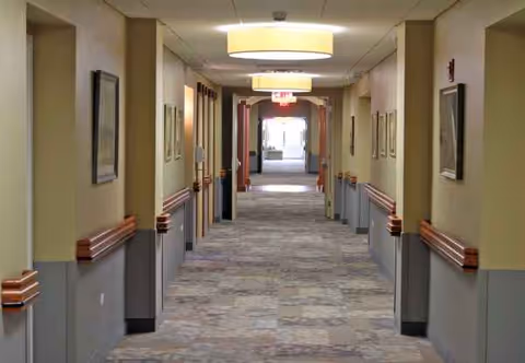 Long hallway in RiverSpring Health facility with framed art, beige walls, and bright ceiling lights.