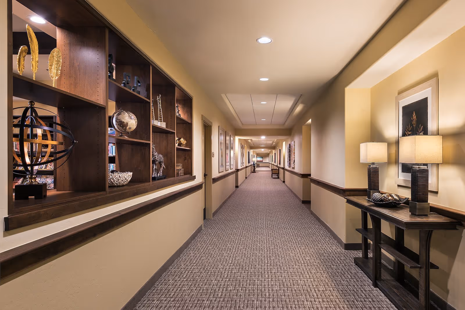Well-lit interior hallway with decorative shelving on the left and a console table with lamps on the right.
