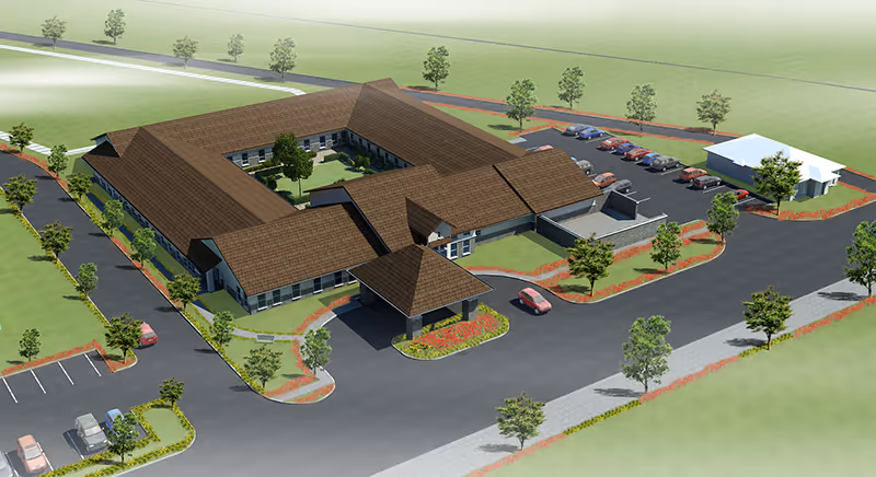Aerial view rendering of The Bradford Memory Care and Assisted Living facility showing a large, single-story building with a brown roof arranged in a U-shape around a central courtyard. The facility is surrounded by parking lots with several cars parked, landscaped areas with trees and shrubs, and paved roads.