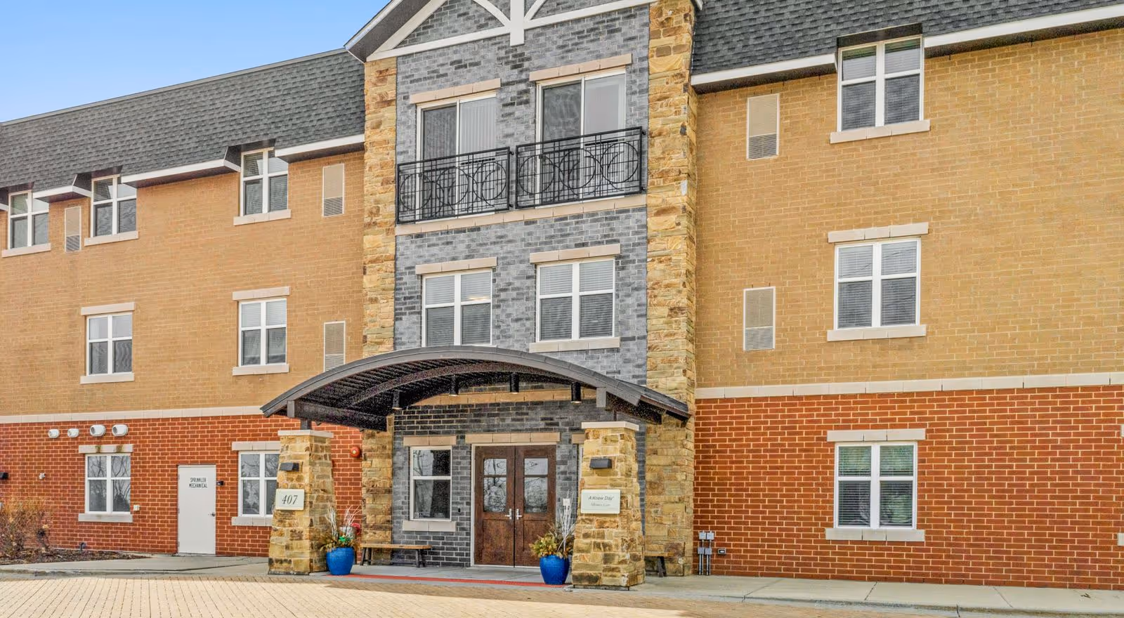 Three-story brick and stone building front with a covered entrance, double doors, windows, and a small decorative balcony.