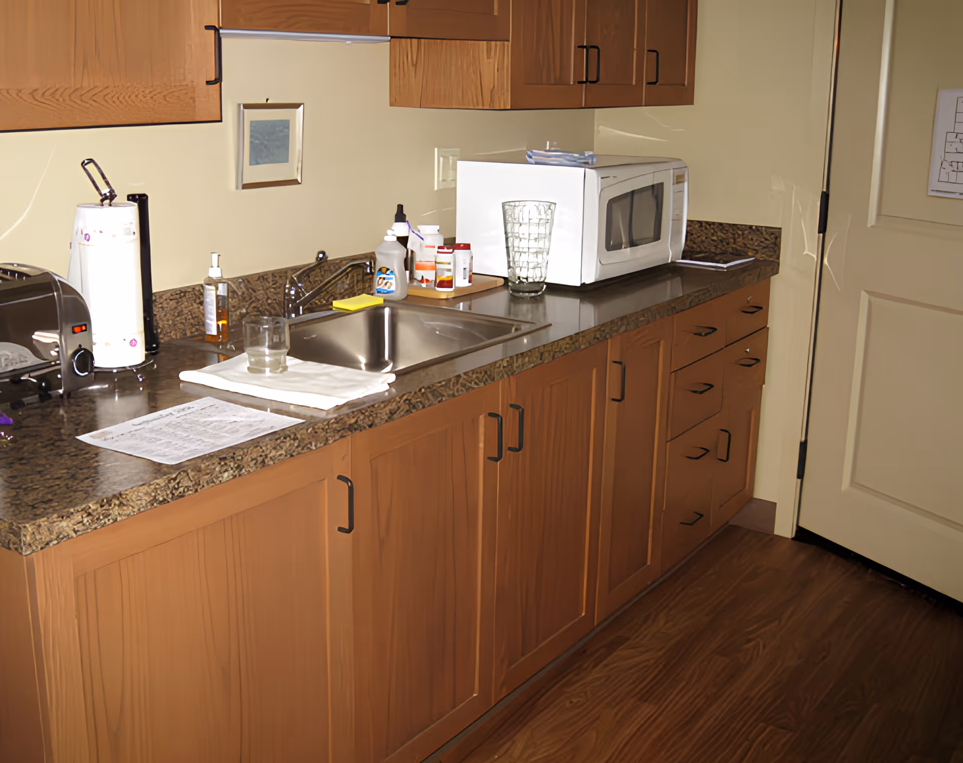 Small kitchen area with wooden cabinets, a sink, microwave, toaster and various countertop items.