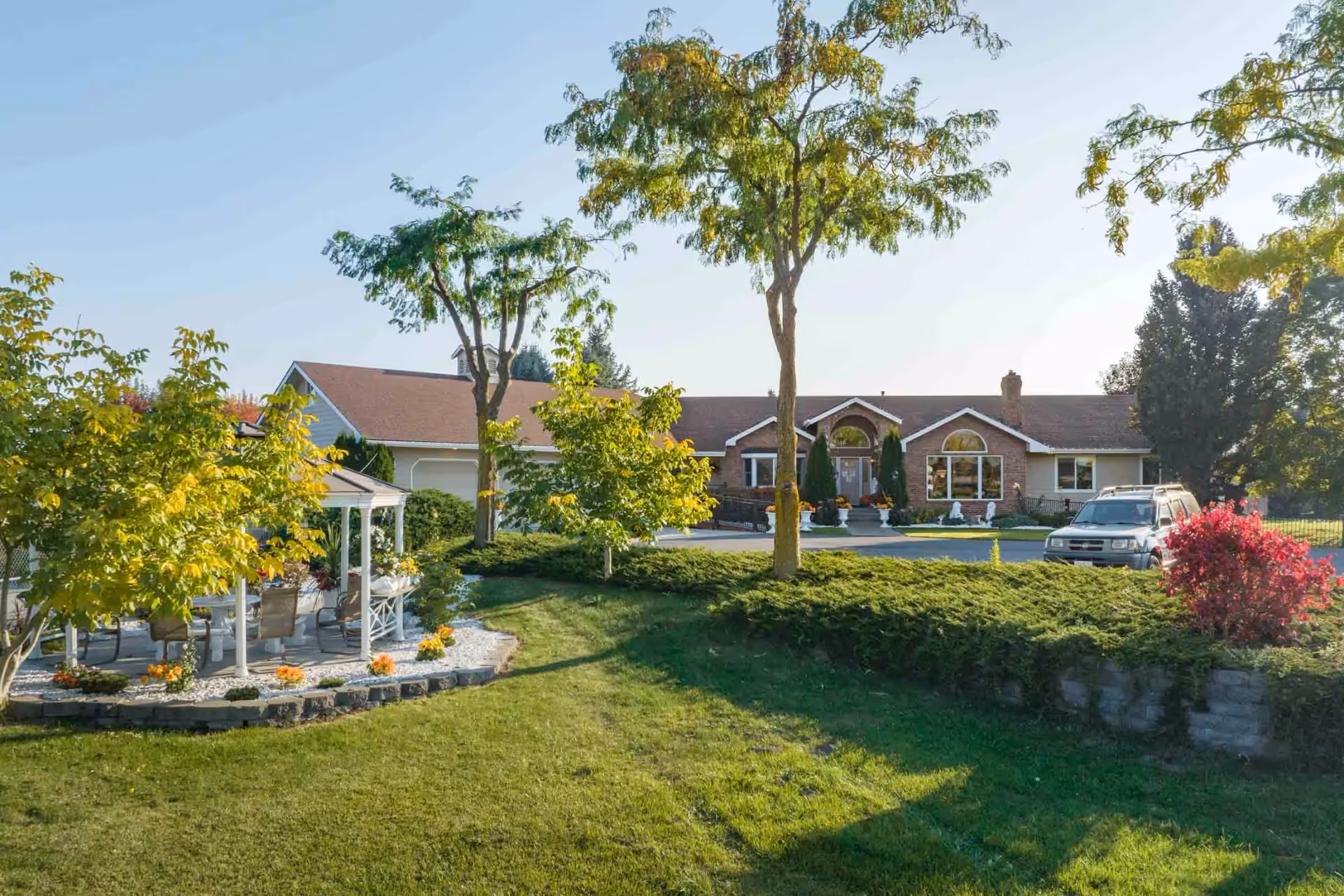 A single-story brick senior living home with a well-kept front lawn, trees, and a white gazebo in the yard.