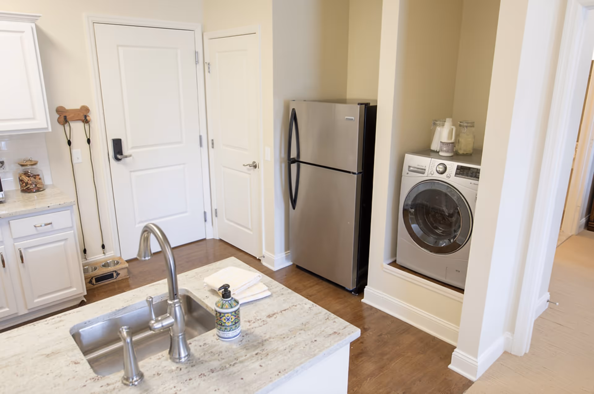 Bright kitchen with an island sink in the foreground, a stainless steel refrigerator and a recessed front‑loading washer in the background, and white cabinetry.