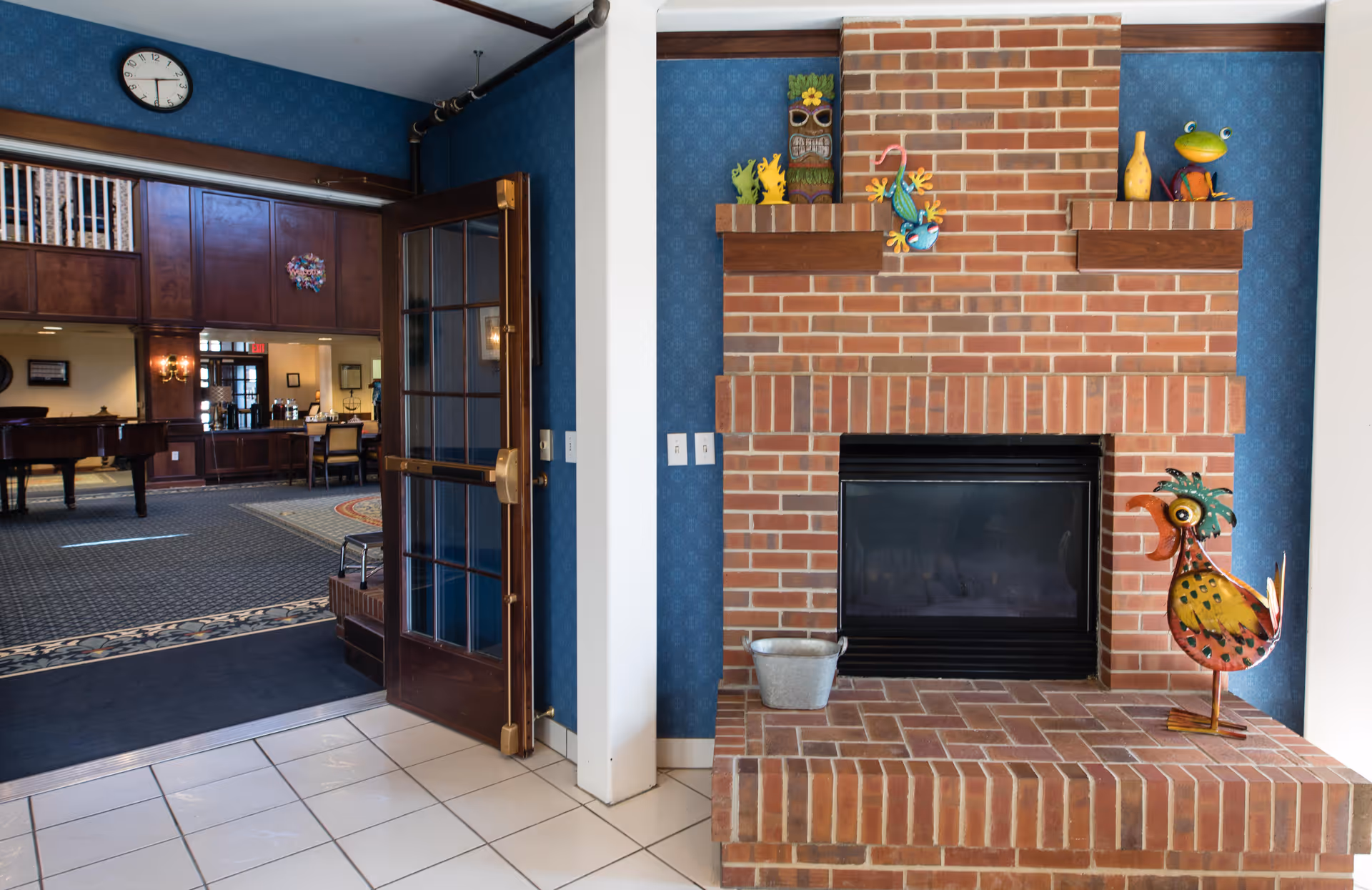Brick fireplace with decorative figurines beside an open glass door leading into a lounge area with a piano and seating.