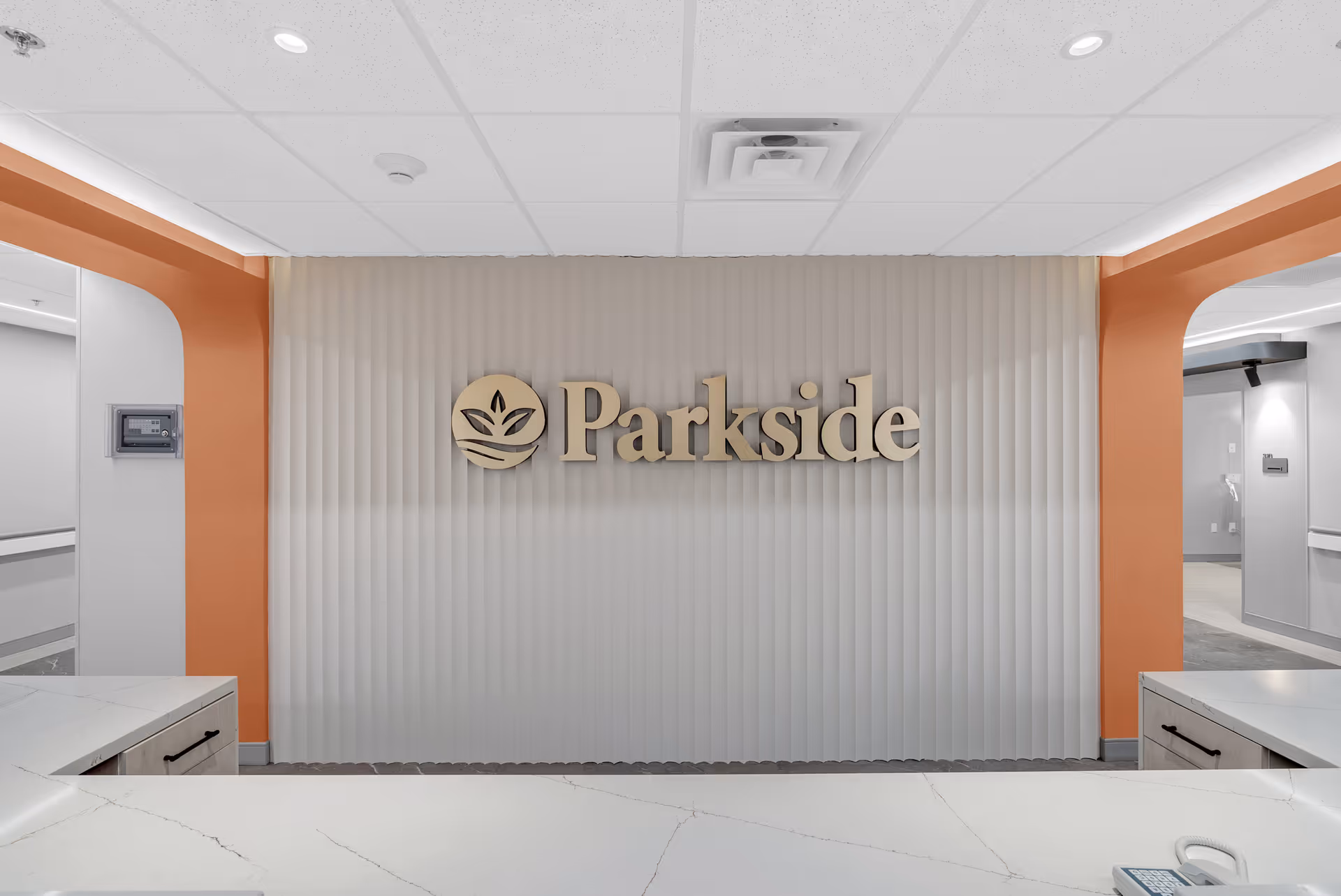 Reception area with a 'Parkside' logo mounted on a ribbed wall behind a white countertop and orange archways.