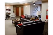 Communal lounge with sofas, armchairs, coffee table, lamps and wall art in a senior living facility interior.