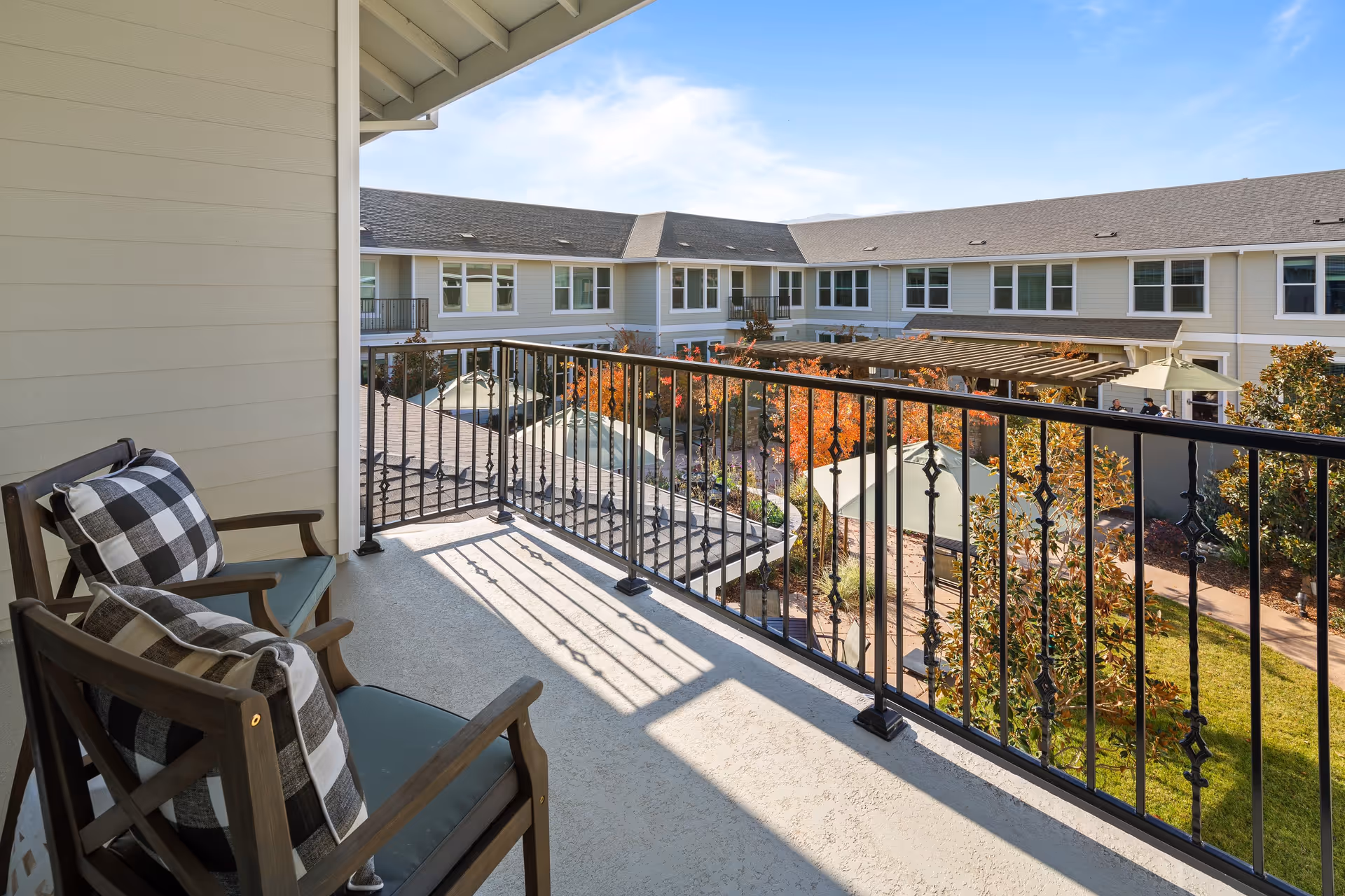 Balcony with two chairs overlooking a landscaped courtyard and surrounding multi-story senior living building.