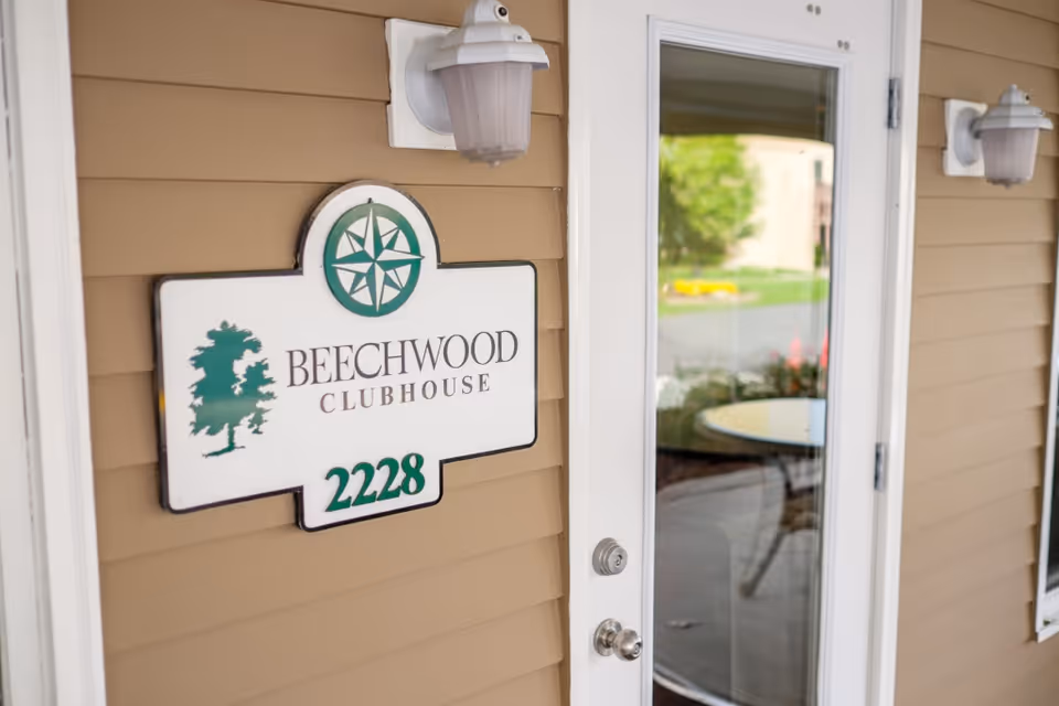 Exterior entrance door with a Beechwood Clubhouse sign reading 2228 mounted on tan siding.