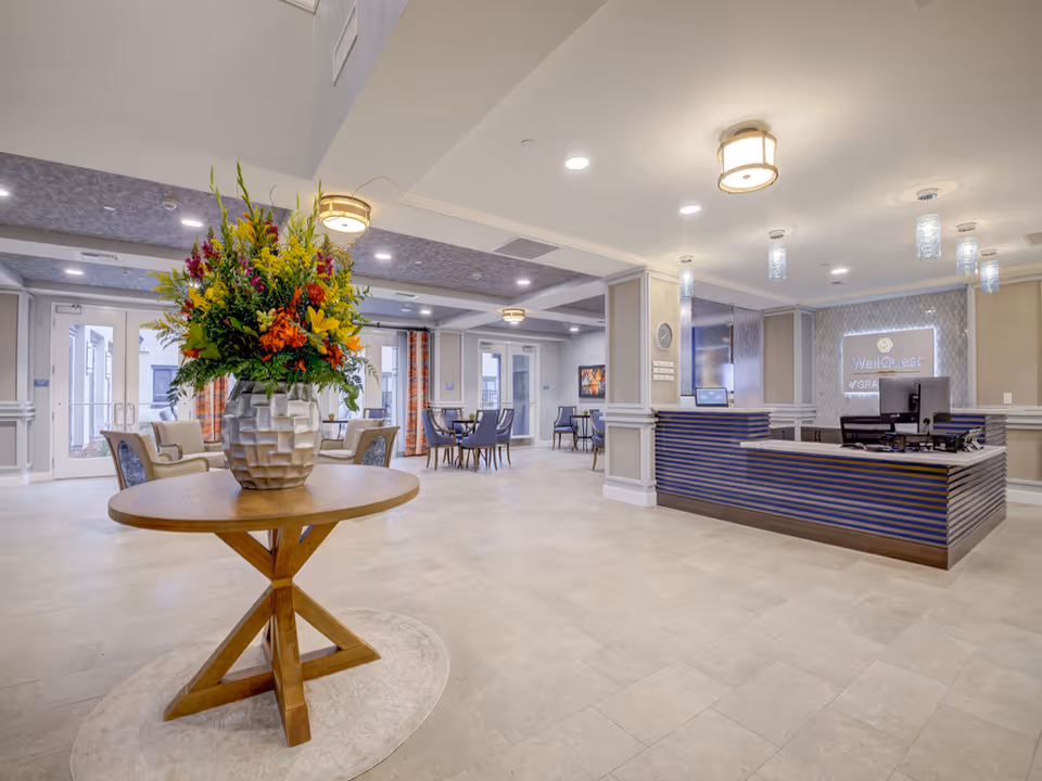 Spacious senior living lobby with a round table holding a large floral arrangement and a reception desk to the right.
