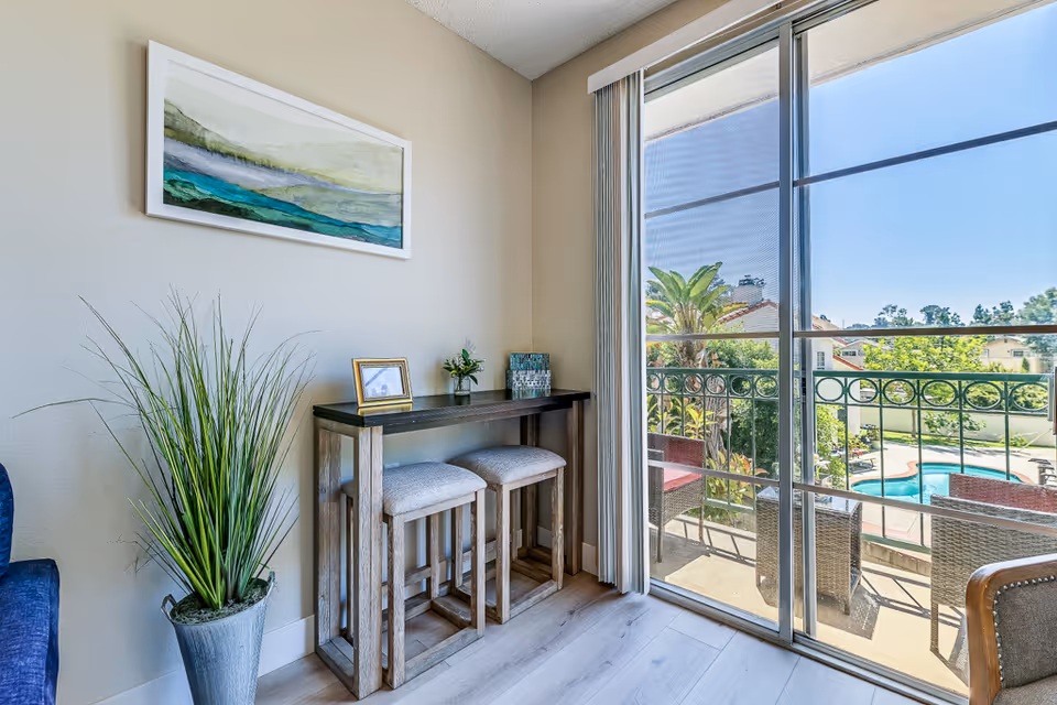 Cozy interior corner with a high table, stools, art, and balcony view of pool.