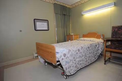A single medical-style bedroom with a bed, nightstand, curtain, and overhead light.