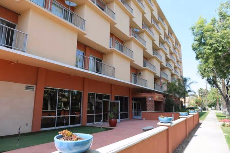 Exterior view of a multi-story senior living building with balconies and a walkway.