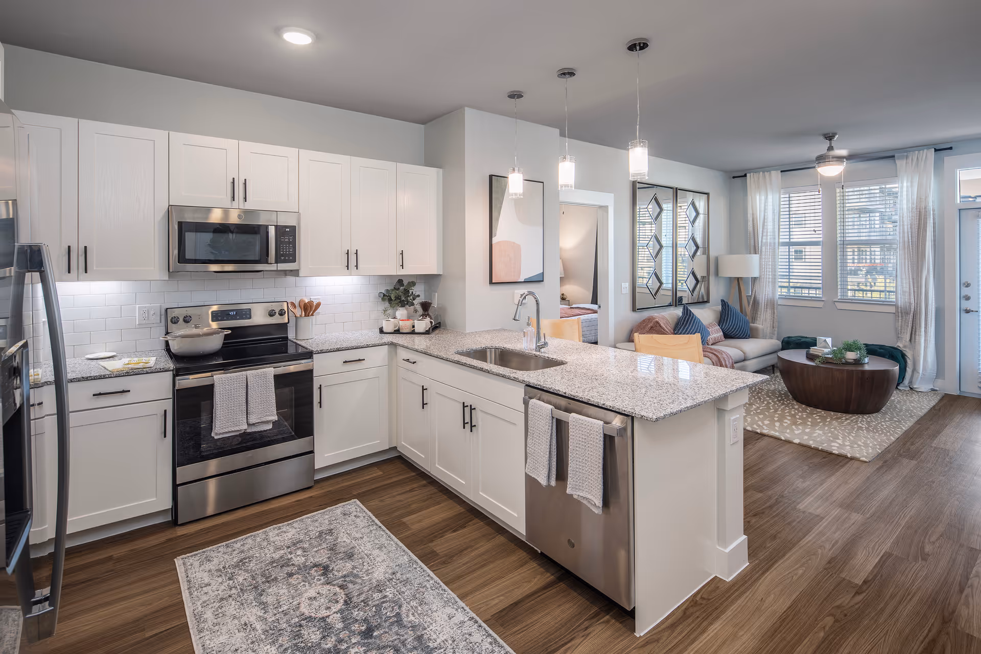Open-plan kitchen with white cabinets, a granite island and stainless steel appliances adjoining a furnished living room.