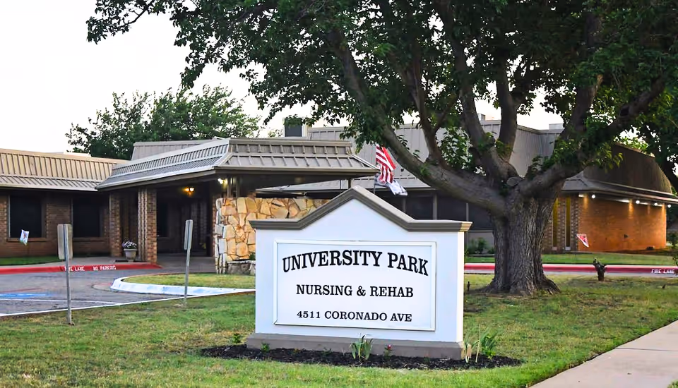 Sign reading University Park Nursing & Rehab in front of the facility's entrance with a large tree and building behind it.