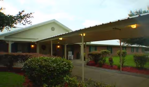 Wide view of Madisonville Assisted Living building exterior with a covered entrance and landscaping.
