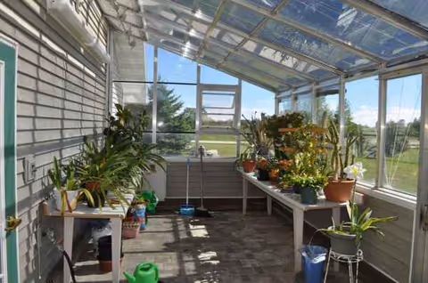 Glass-enclosed sunroom with potted plants on tables and cleaning supplies.