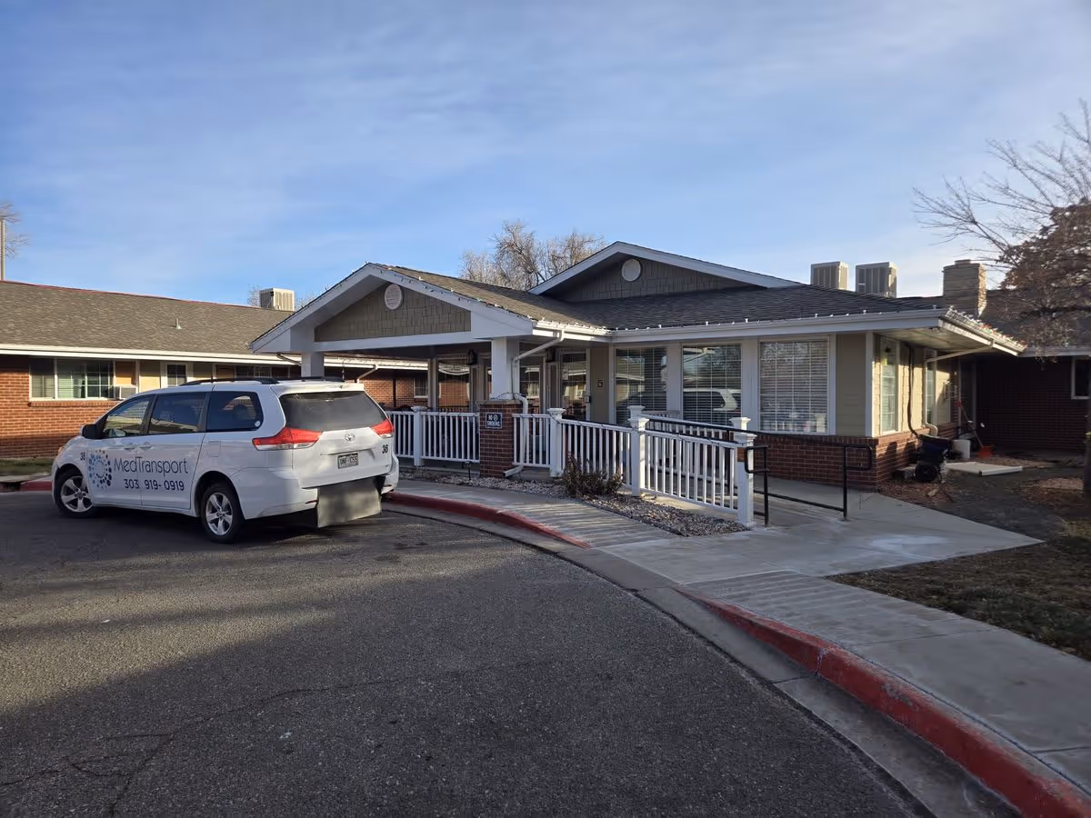 Front entrance of a single-story facility with a covered entry, wheelchair ramp, and a parked MediTransport van.