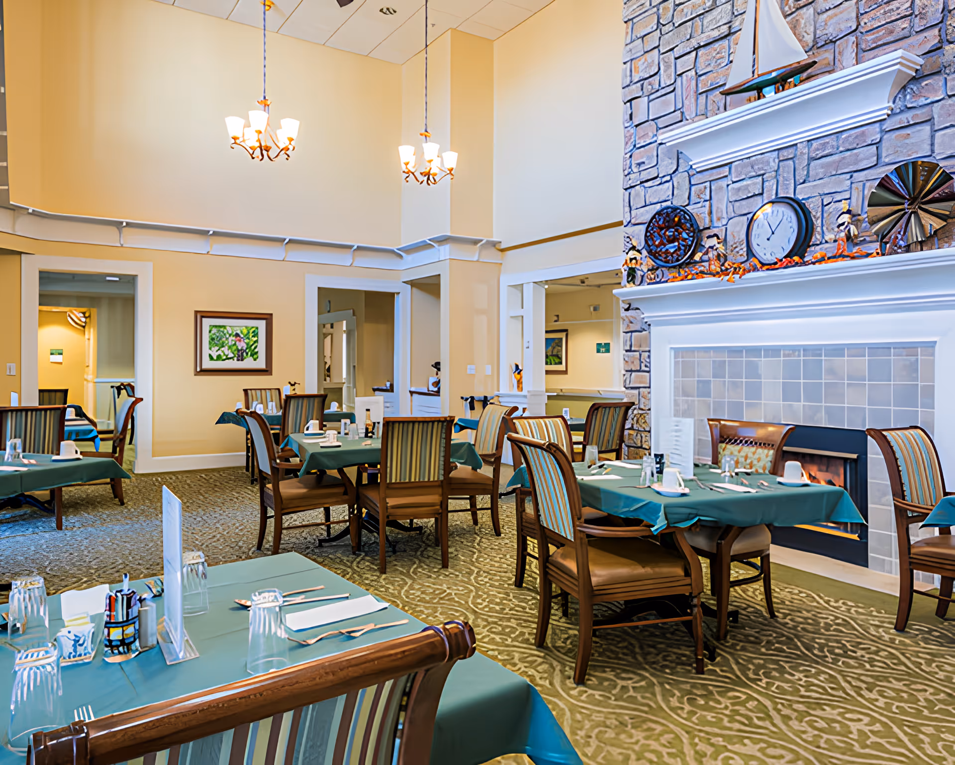 Dining room with multiple tables set for meals, a fireplace, and high ceilings with chandeliers.