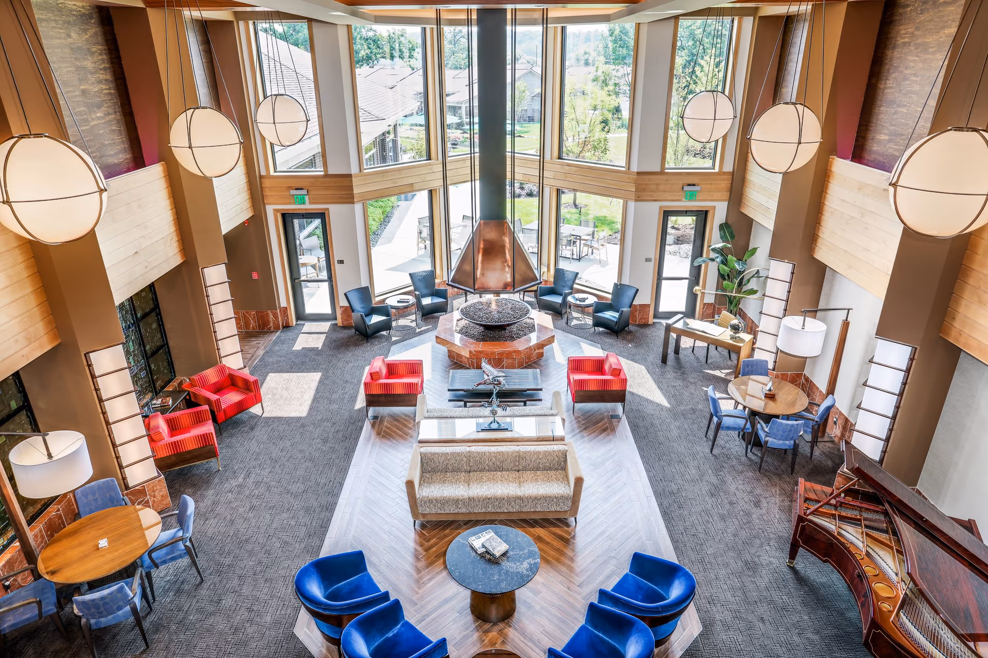 Sunlit two-story communal lounge with multiple seating areas, a central fireplace, large windows and hanging globe lights.