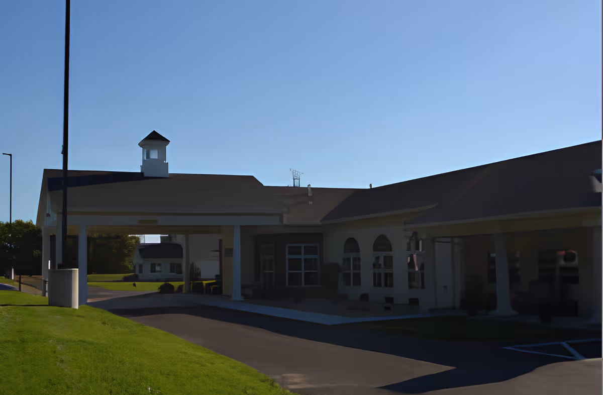 Exterior view of Centreville Village Assisted Living showing the front entrance with a covered driveway, white pillars, and a small cupola on the roof under a clear blue sky.