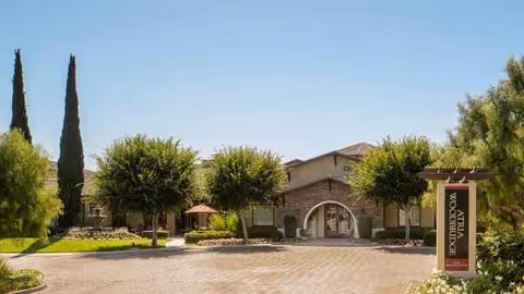 Exterior view of Woodbridge Terrace senior living facility entrance with trees and a sign.