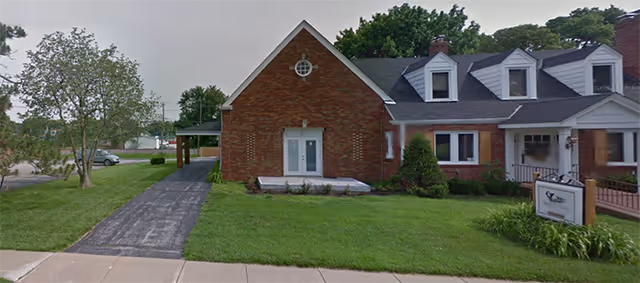Brick senior living facility front exterior with lawn, walkway, and sign.