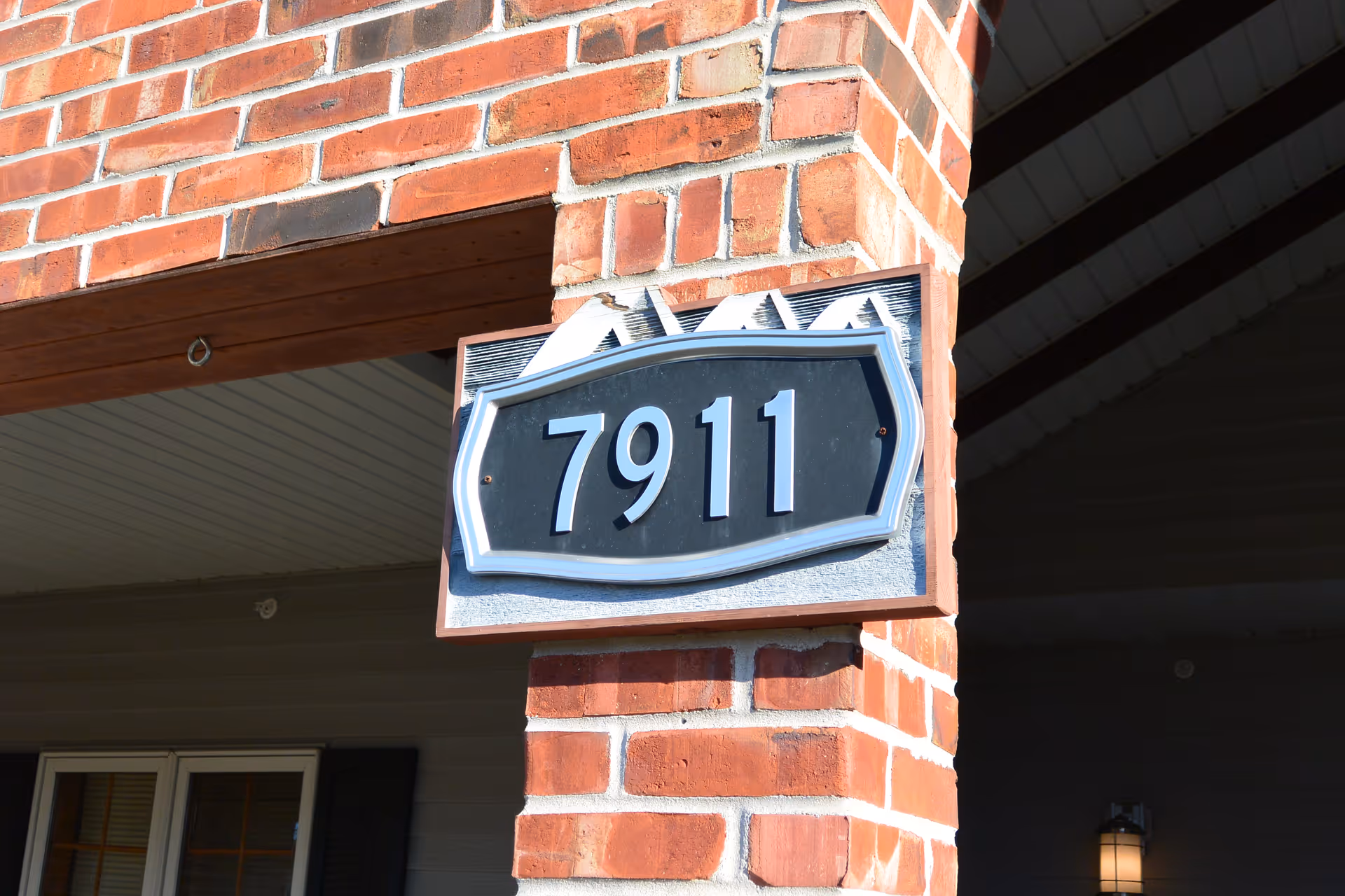 A black house number plaque reading "7911" mounted on a brick column under a porch.