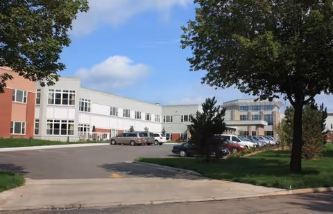 Exterior view of PioneerCare Center with parking lot, cars, and trees.