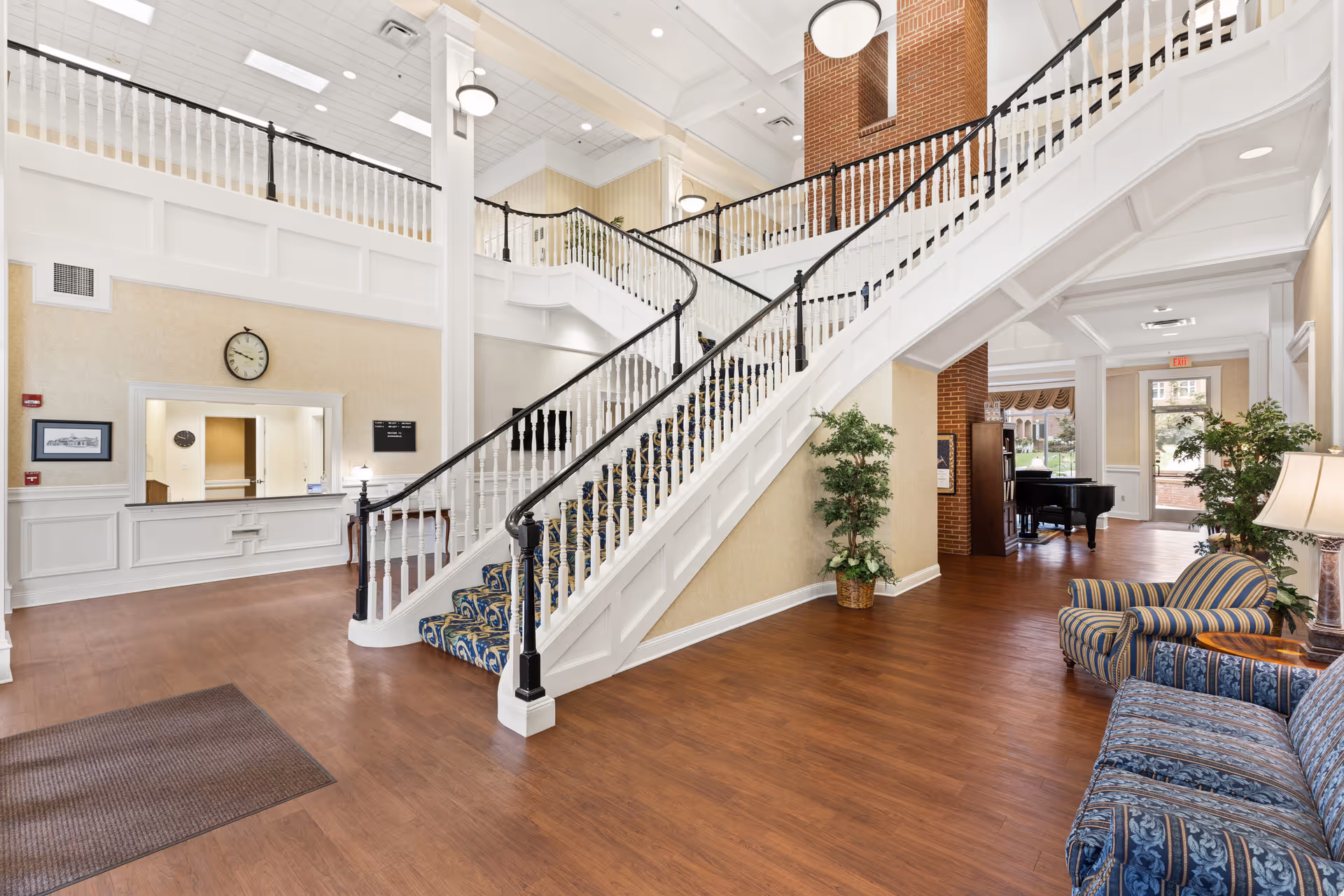 Bright two-story lobby with a sweeping white staircase, seating area, and a reception desk.