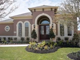 Front exterior view of a single-story building with a large arched entrance, tall narrow windows, and a well-maintained lawn with landscaping including small trees and shrubs.