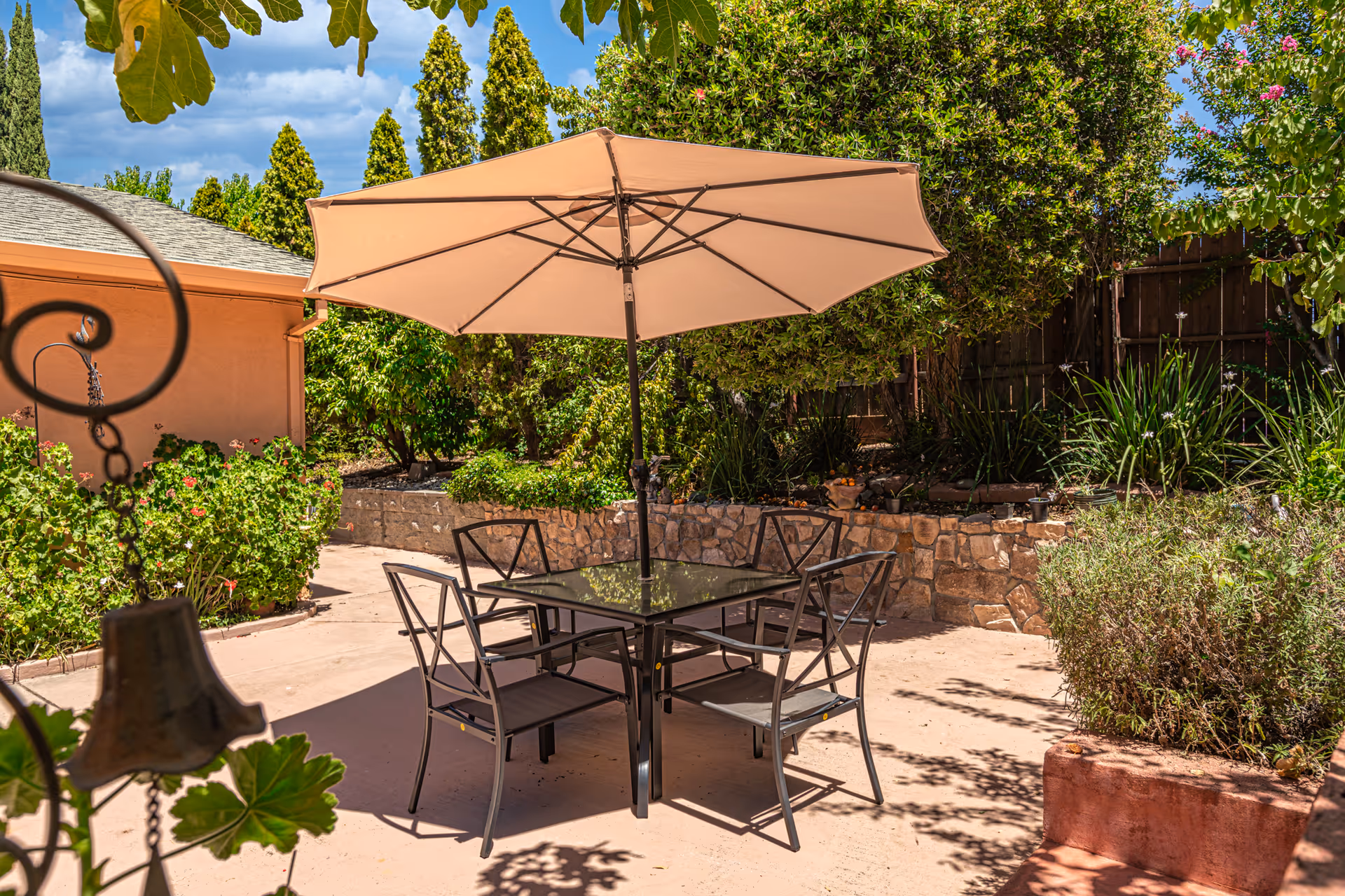Outdoor patio with a table, umbrella, and chairs surrounded by greenery and stone planters.