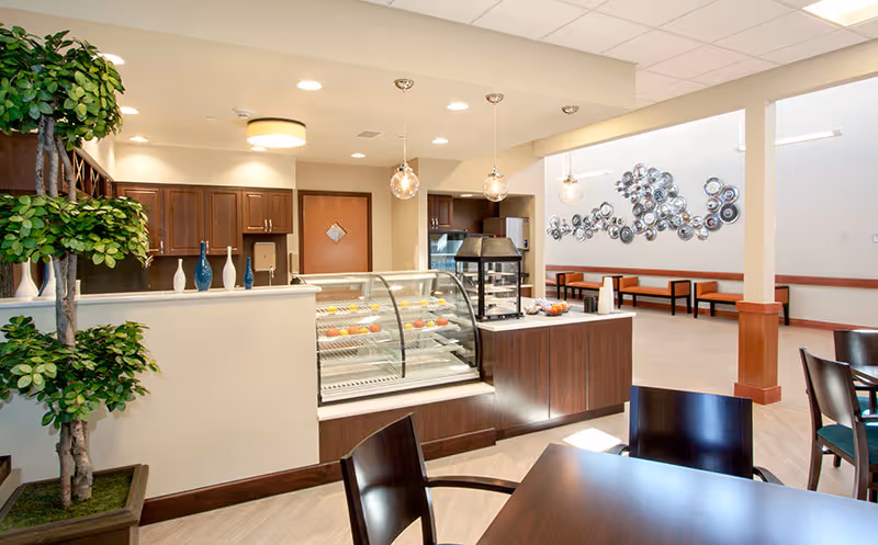 Bright dining/lounge area with a glass pastry display case, seating, modern pendant lights, and decorative wall art.
