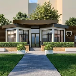 Front entrance of a modern rehabilitation facility with glass doors, symmetrical planters, a paved walkway and a heart logo on a wooden exterior wall.