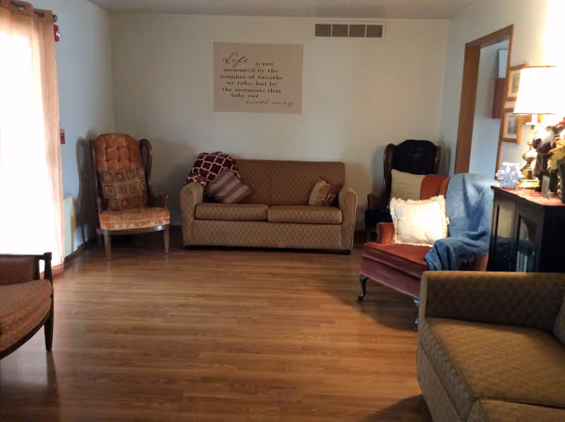 A spacious living-room seating area with sofas, armchairs, hardwood floors and a wall sign.