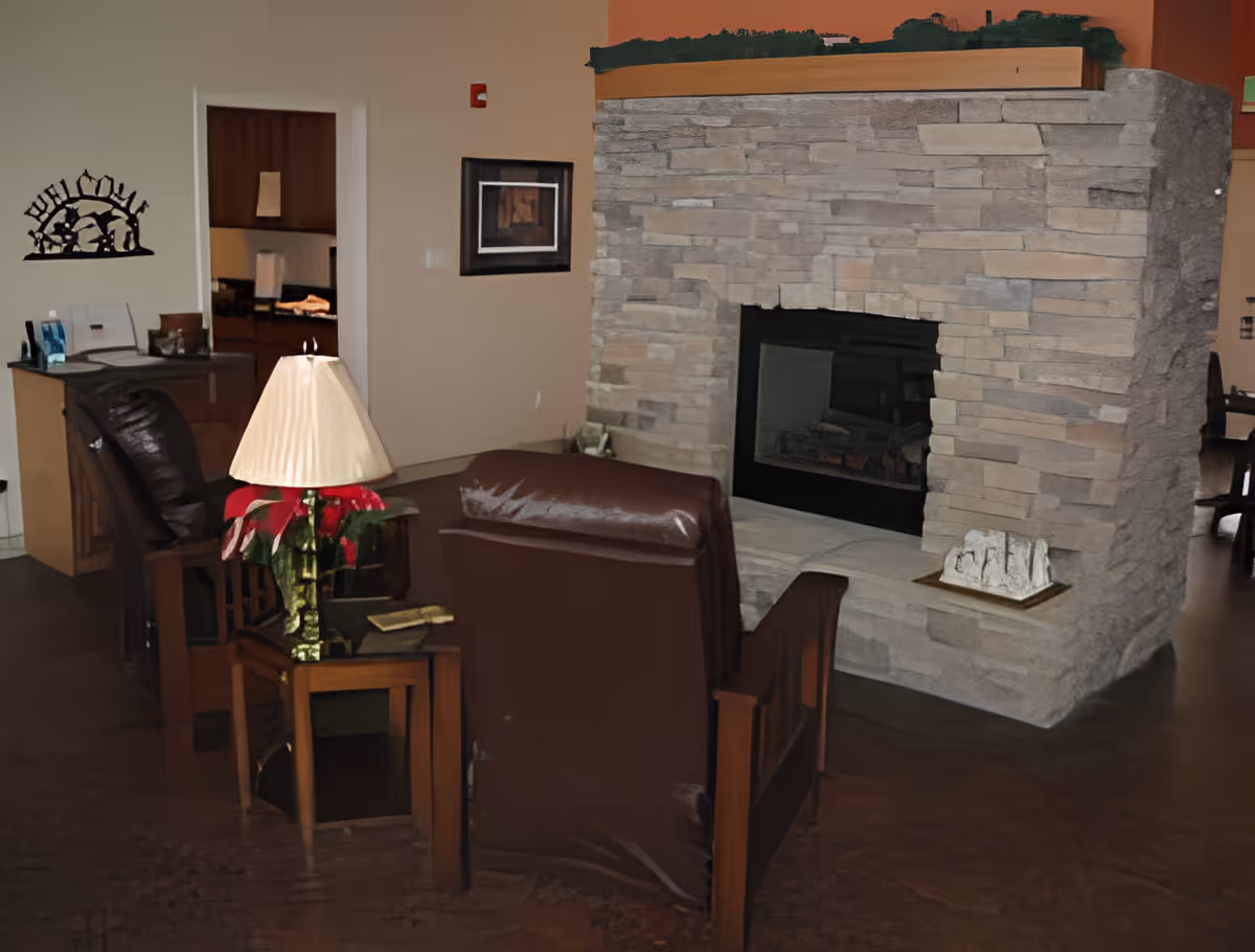 Cozy common living area with leather chairs, side tables, a lamp, and a large stone fireplace.