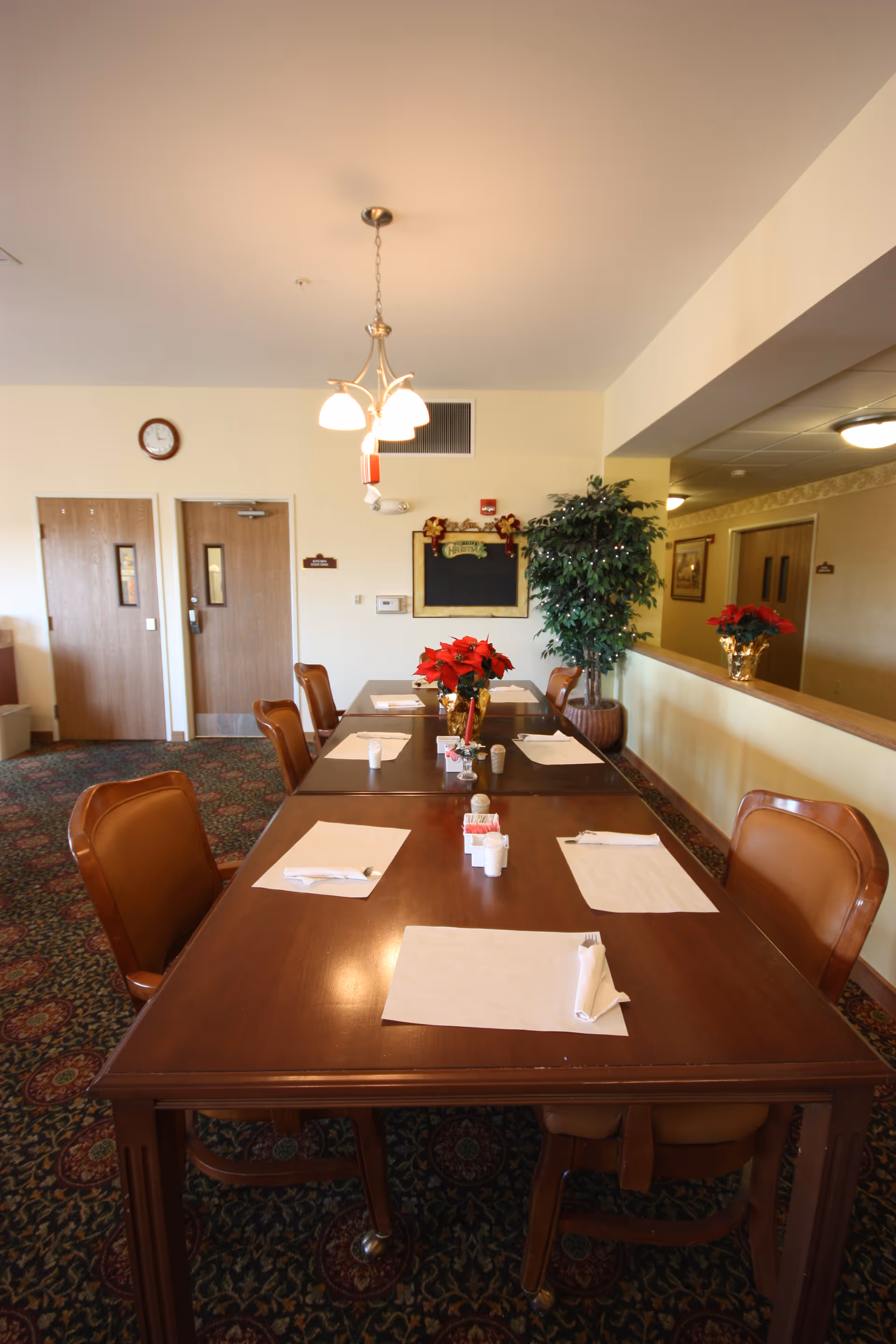 Long wooden dining table with placemats and poinsettia centerpieces in a senior living dining room.