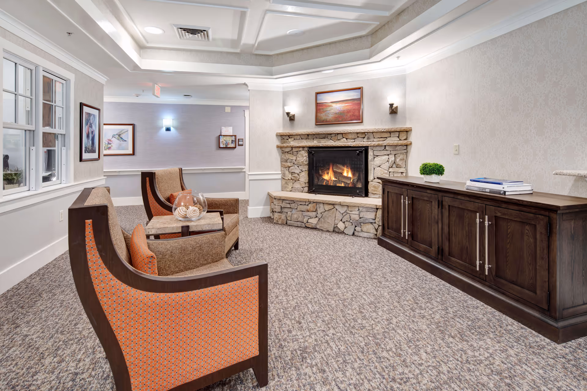 Cozy lounge area with upholstered chairs, a stone fireplace, and a wooden cabinet in a communal room.