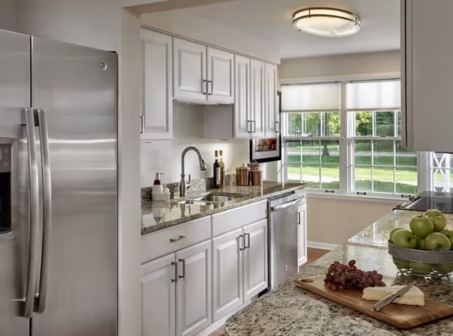 Bright kitchen with white cabinets, granite countertops, stainless steel appliances, and a window overlooking a green lawn.