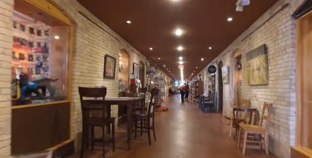 Long indoor brick hallway with tables, chairs and display cases along both sides and people in the distance.
