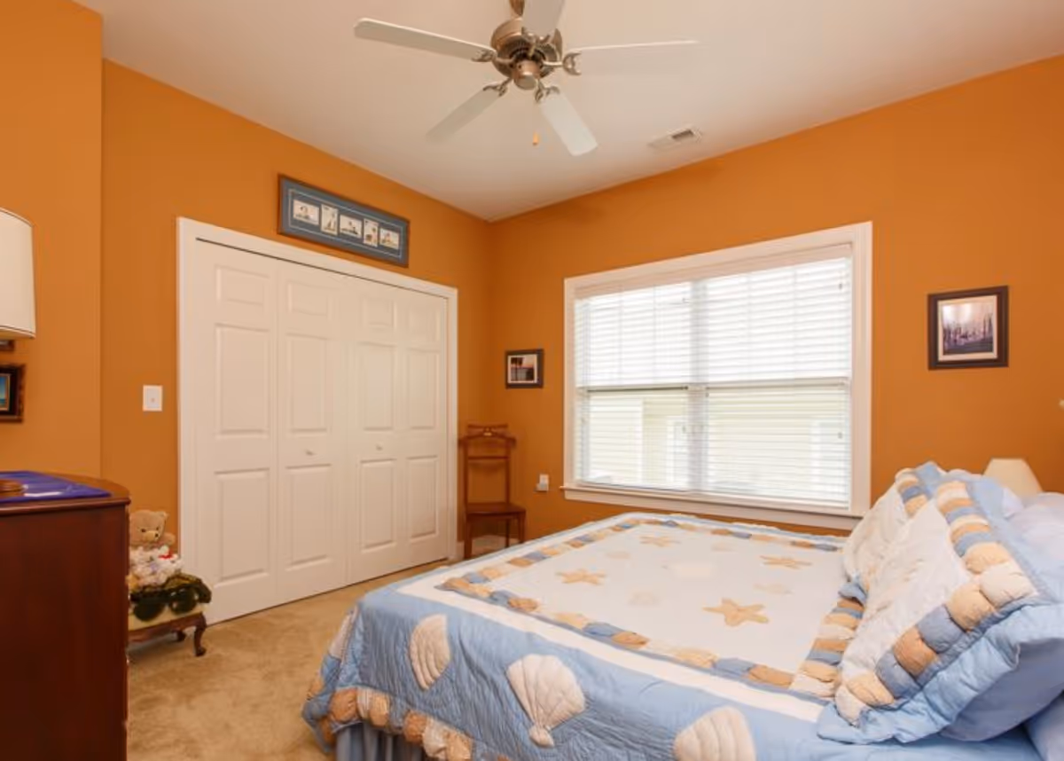 Bedroom with a seashell-themed quilt on the bed, orange walls, a window with blinds, ceiling fan, and white double closet doors.