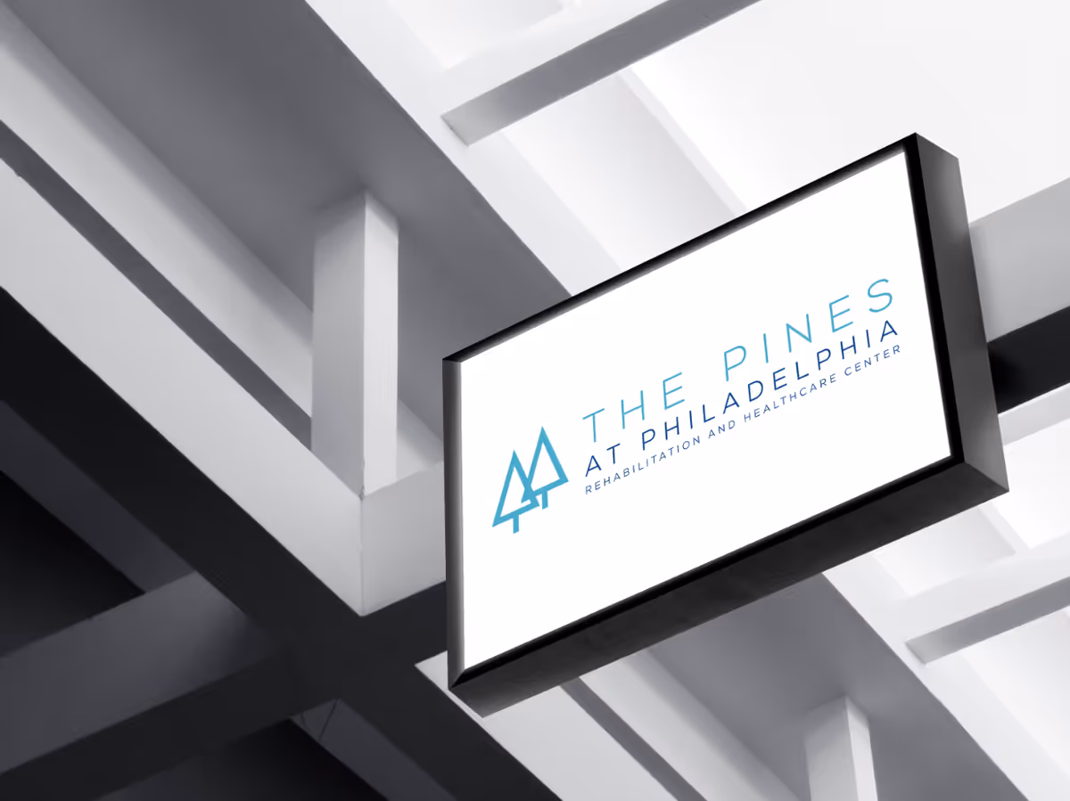 Illuminated hanging sign for The Pines at Philadelphia rehabilitation and healthcare center suspended from a white geometric ceiling.