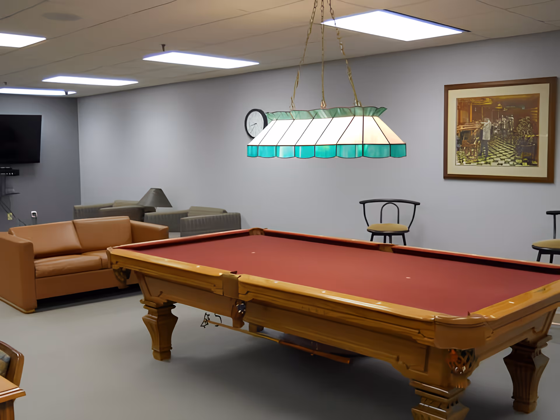 Indoor recreation room with a red-felt pool table, hanging stained-glass light, sofas and a wall-mounted TV.