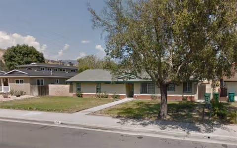 Single-story building with green trim, front yard, and a tree beside the street.