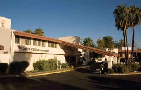 Exterior view of The Gardens at Immanuel facility with palm trees and parked cars.