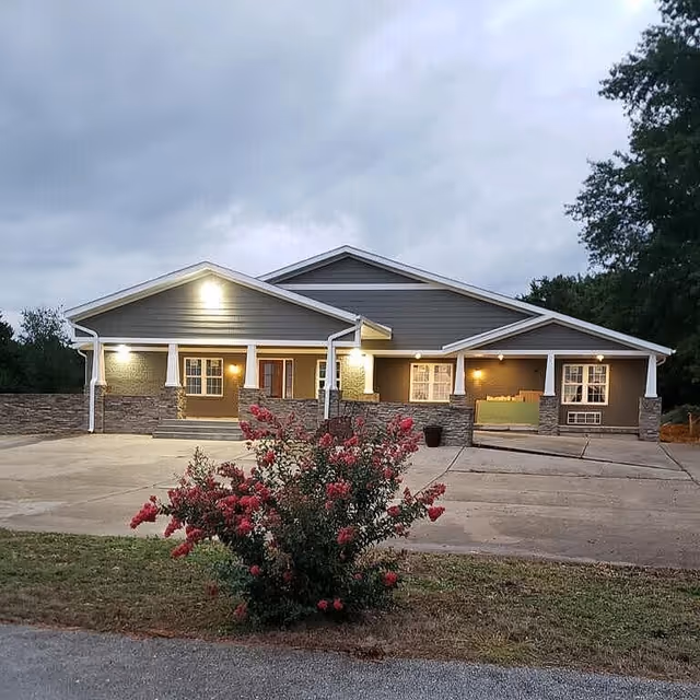 Front exterior view of The Oaks Cottage senior living facility with a flowering bush in the foreground.